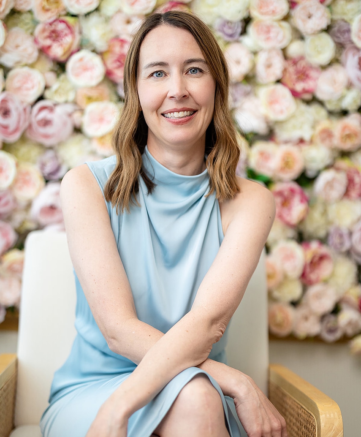 Woman in light blue dress, smiling near flowers.
