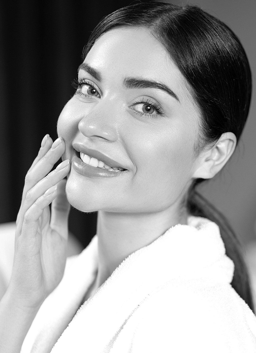Woman smiling in a robe, touching her face.