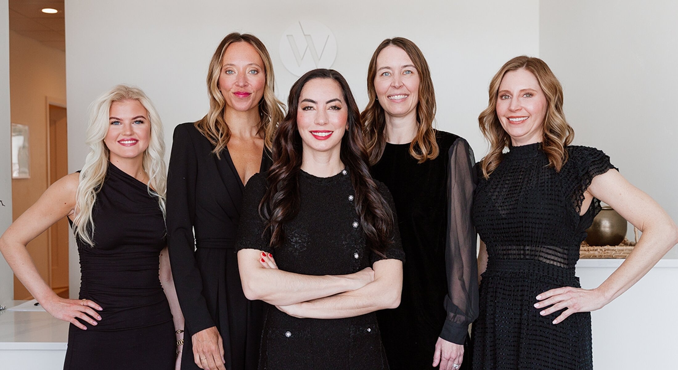 Five women posing in stylish black outfits.
